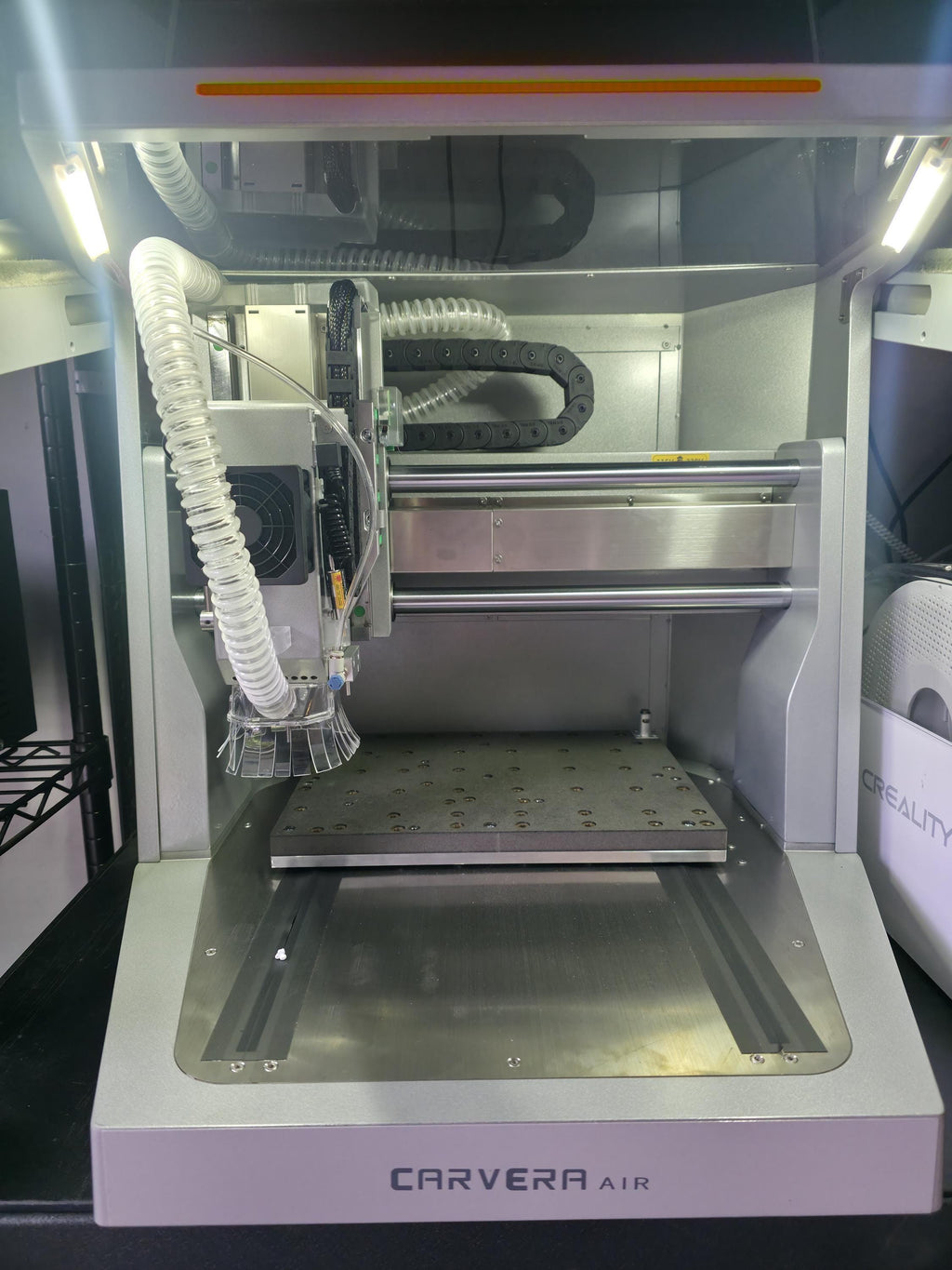 Inside view of a Carvera Air CNC machine featuring a metal workbed, dust hose, and LED lights. This image emphasizes the technical workspace environment associated with the “OH SH*T BUTTON” accessory.