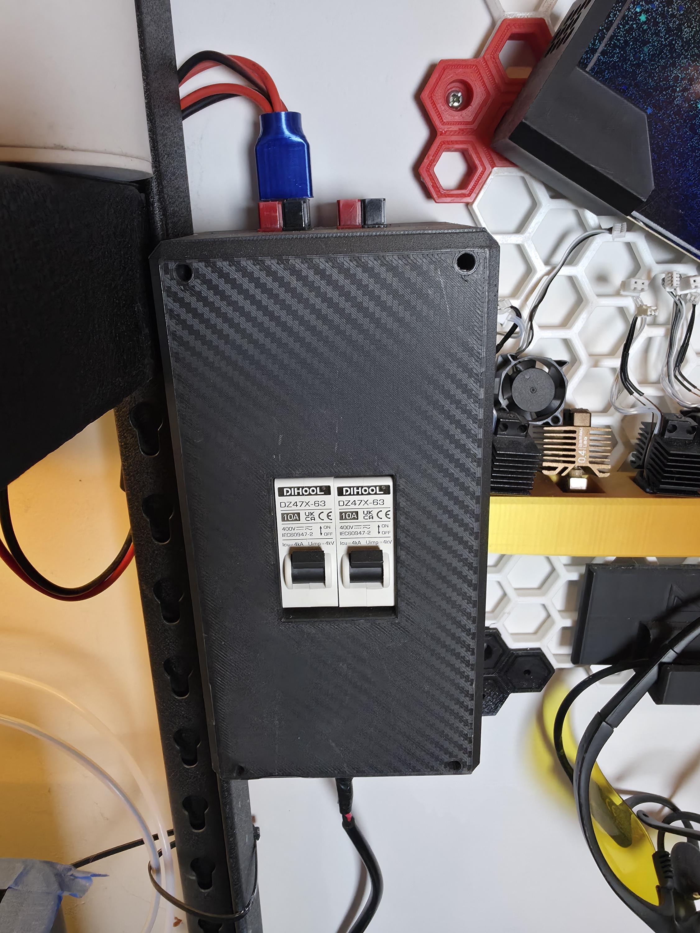 Overhead view of Aetherium DC breaker box showing dual 10A DIHOOL breakers in a carbon fiber polymer housing, top-mounted red and black Powerpole connectors, and side cable routing for neat bench or mobile installation.