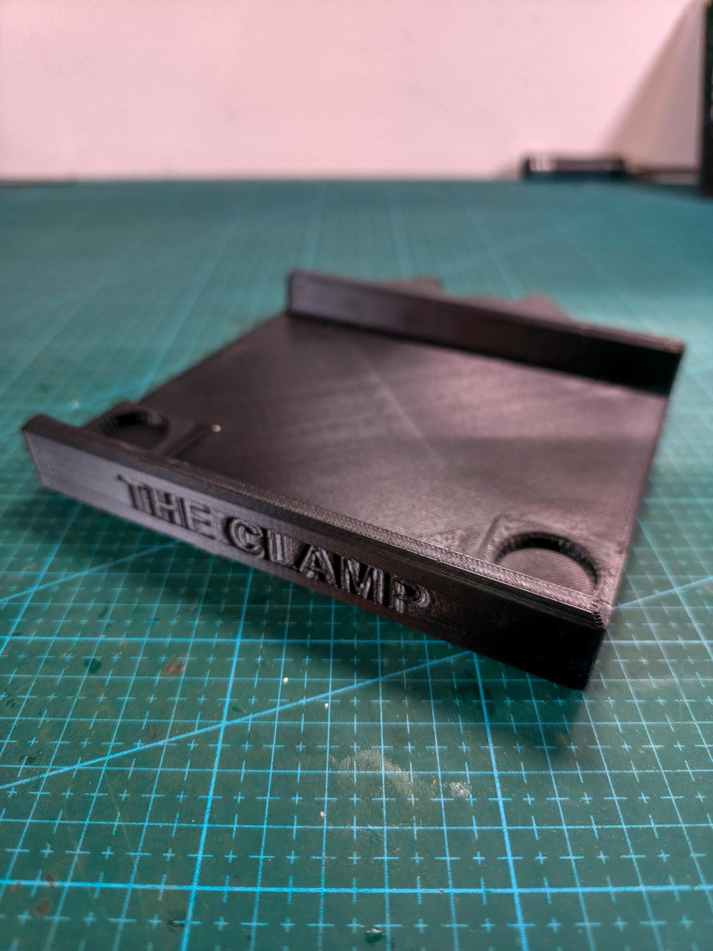 Close-up of the Quick Clamp Adapter base plate, printed in carbon fiber–reinforced polymer with integrated clamp channel and embossed text reading “THE CLAMP.”