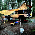 image features a jeep gladiator eco diesel with a super pacific x1 camper and awning set up in the rain. with led lights illuminating the surrounding camp site
