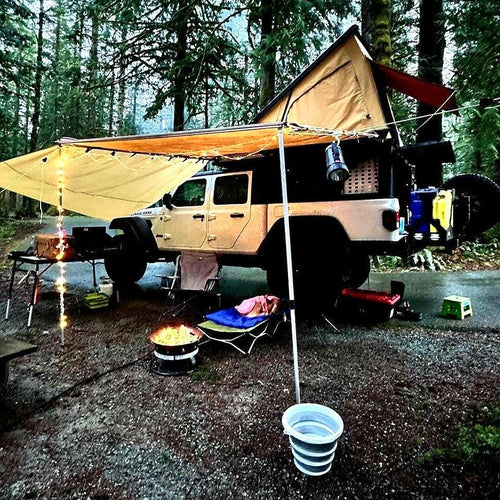 image features a jeep gladiator eco diesel with a super pacific x1 camper and awning set up in the rain. with led lights illuminating the surrounding camp site