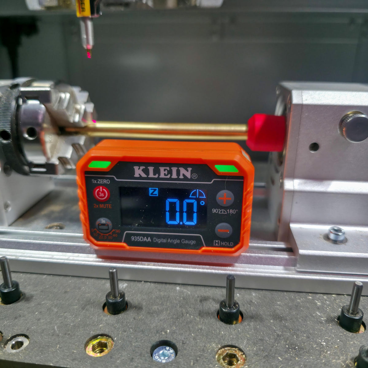 Digital angle gauge reading “0.0” placed between two rotary heads in a CNC machine. The laser probe and red centering jig confirm level alignment before cutting.