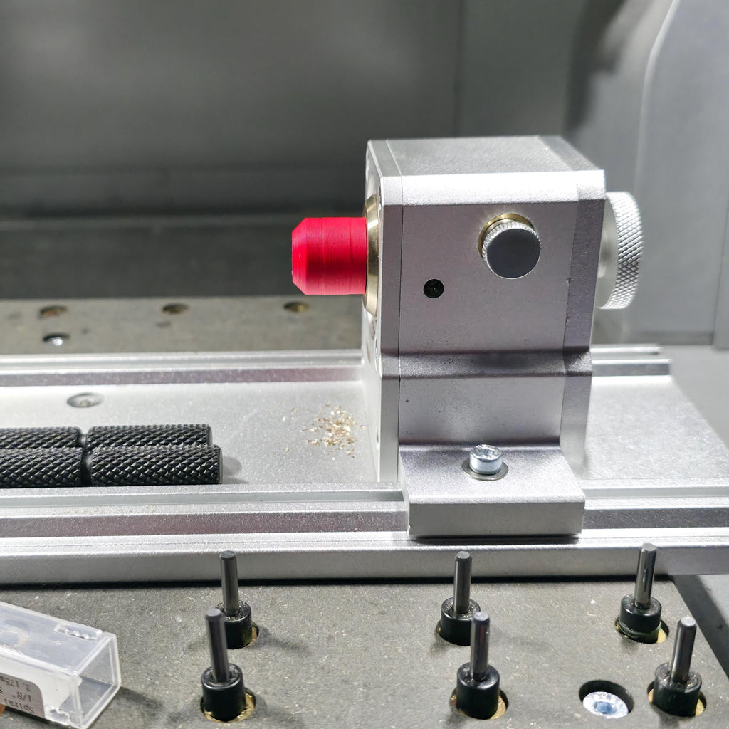 Rotary head assembly on a CNC baseplate fitted with a red alignment jig. Multiple guide pins and fixture bolts are visible, showing a typical maker setup for precision stock alignment.