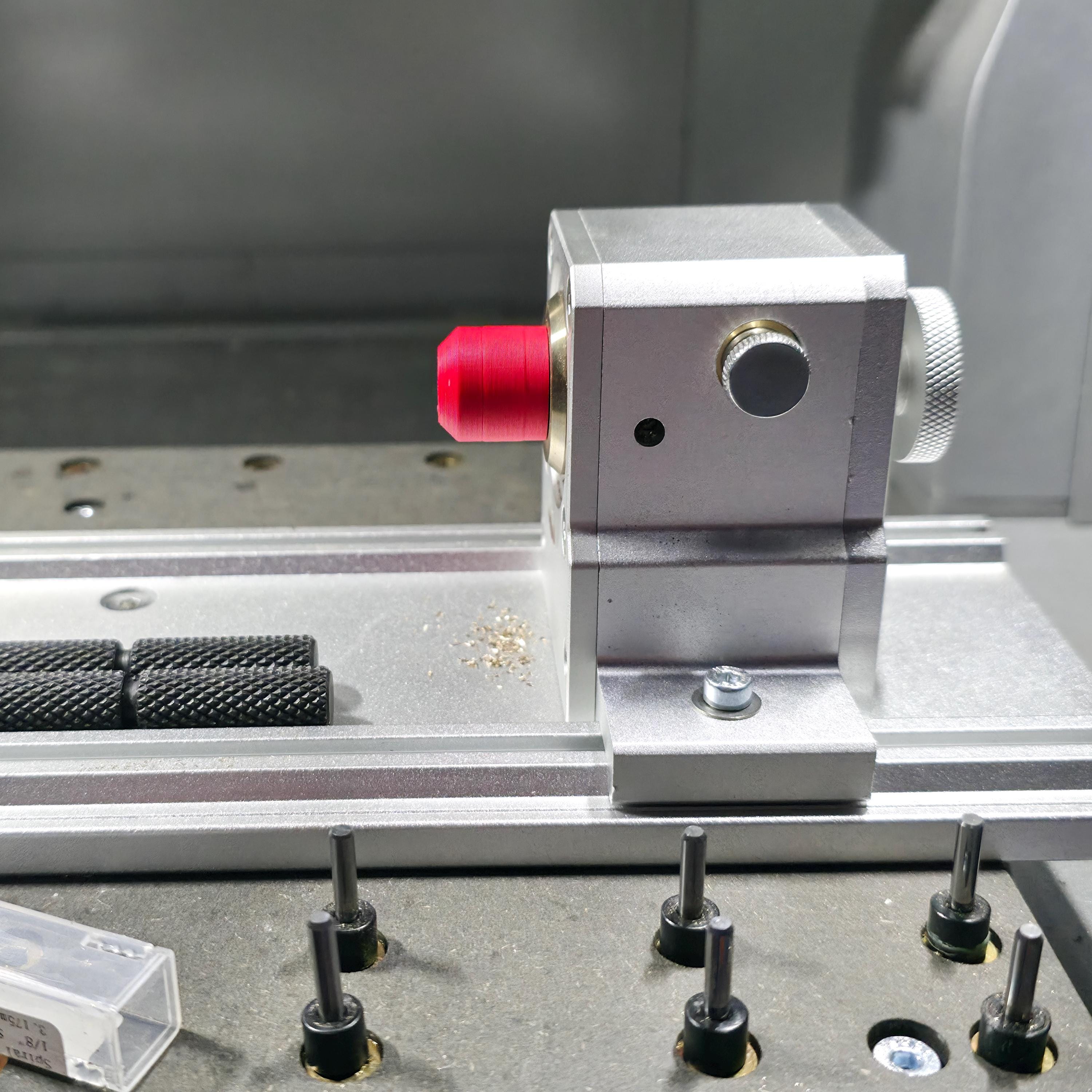 Rotary head assembly on a CNC baseplate fitted with a red alignment jig. Multiple guide pins and fixture bolts are visible, showing a typical maker setup for precision stock alignment.