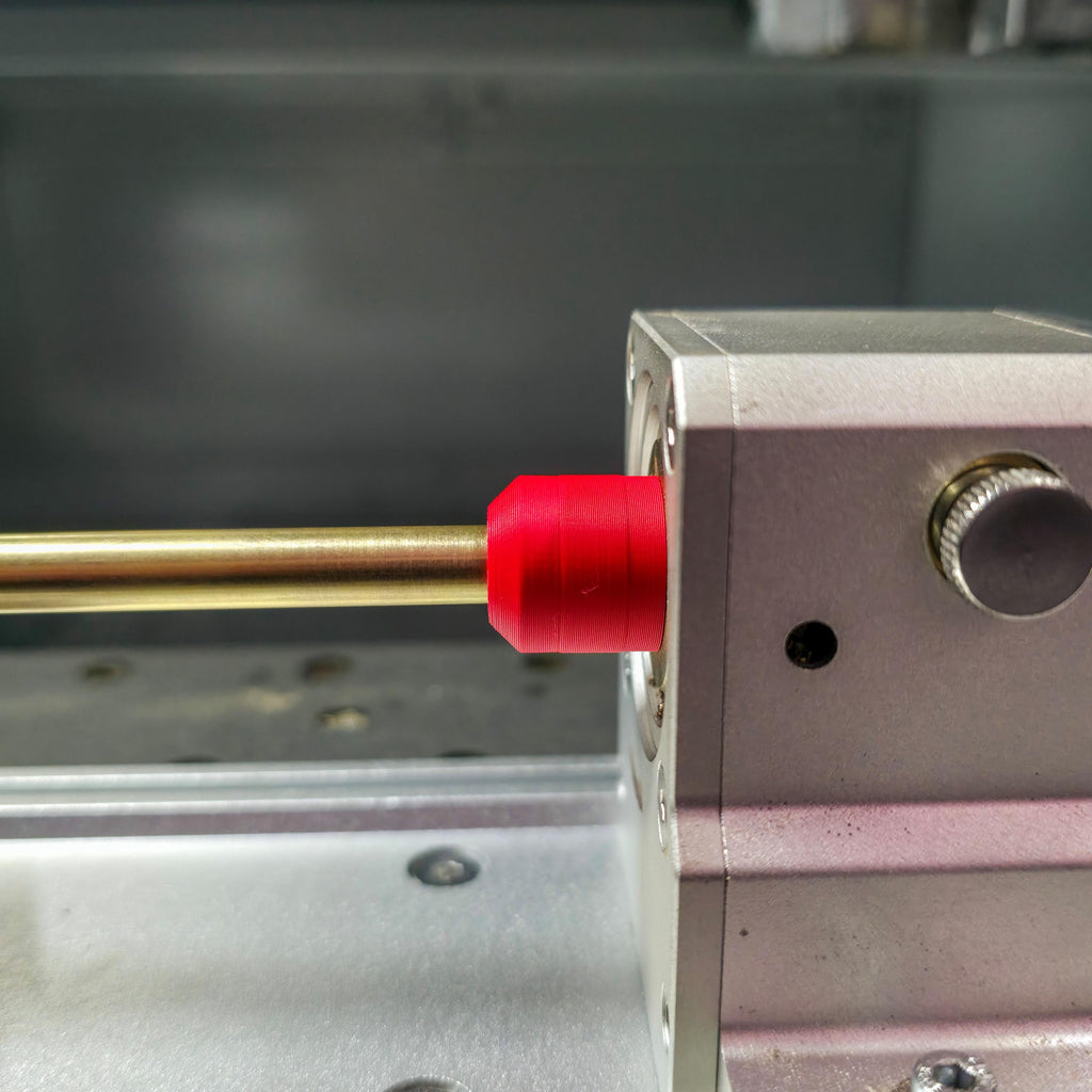 Side view of brass stock secured in a Makera 4th-axis head using a red precision jig. The smooth alignment shows accurate centering for rotary milling or engraving work.