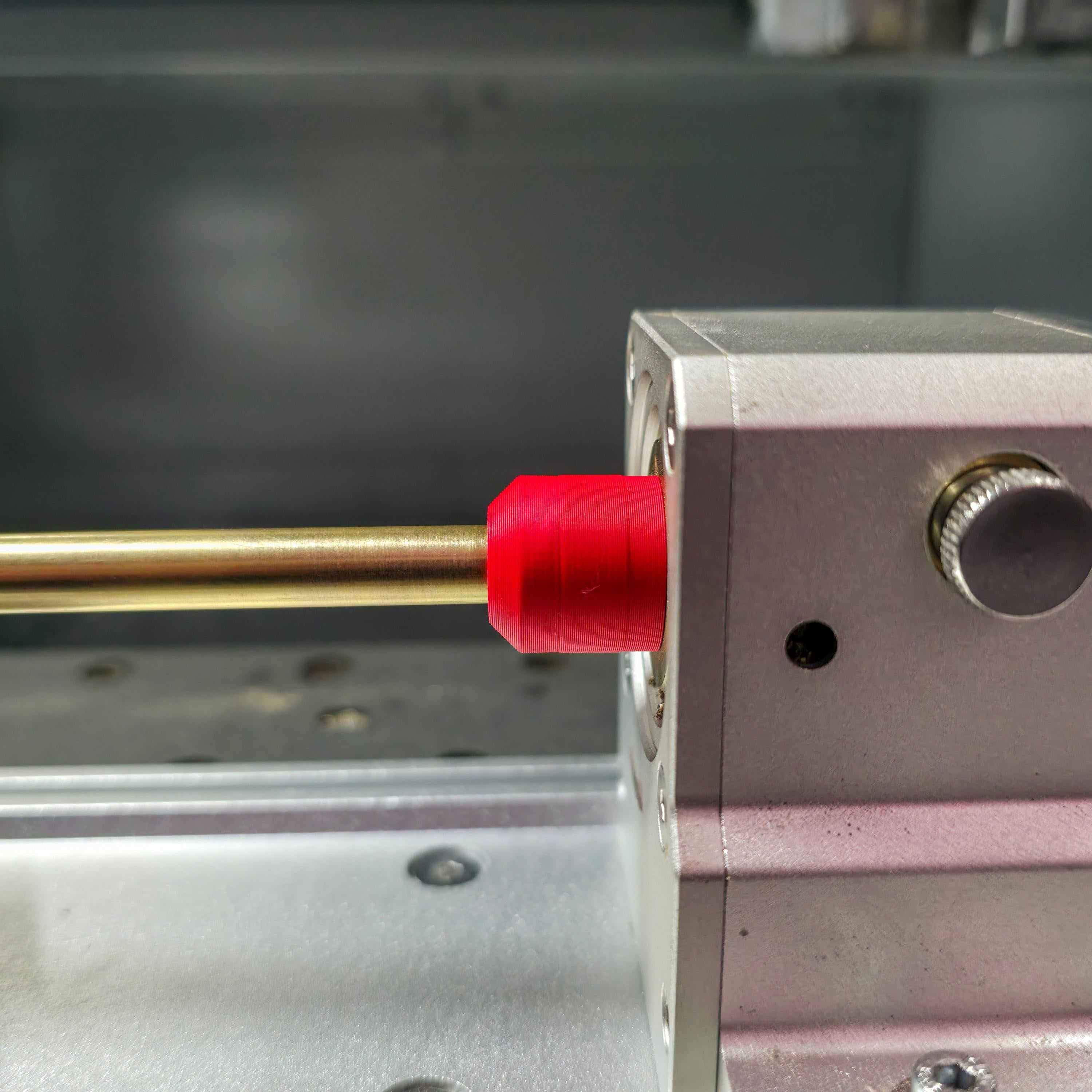 Side view of brass stock secured in a Makera 4th-axis head using a red precision jig. The smooth alignment shows accurate centering for rotary milling or engraving work.
