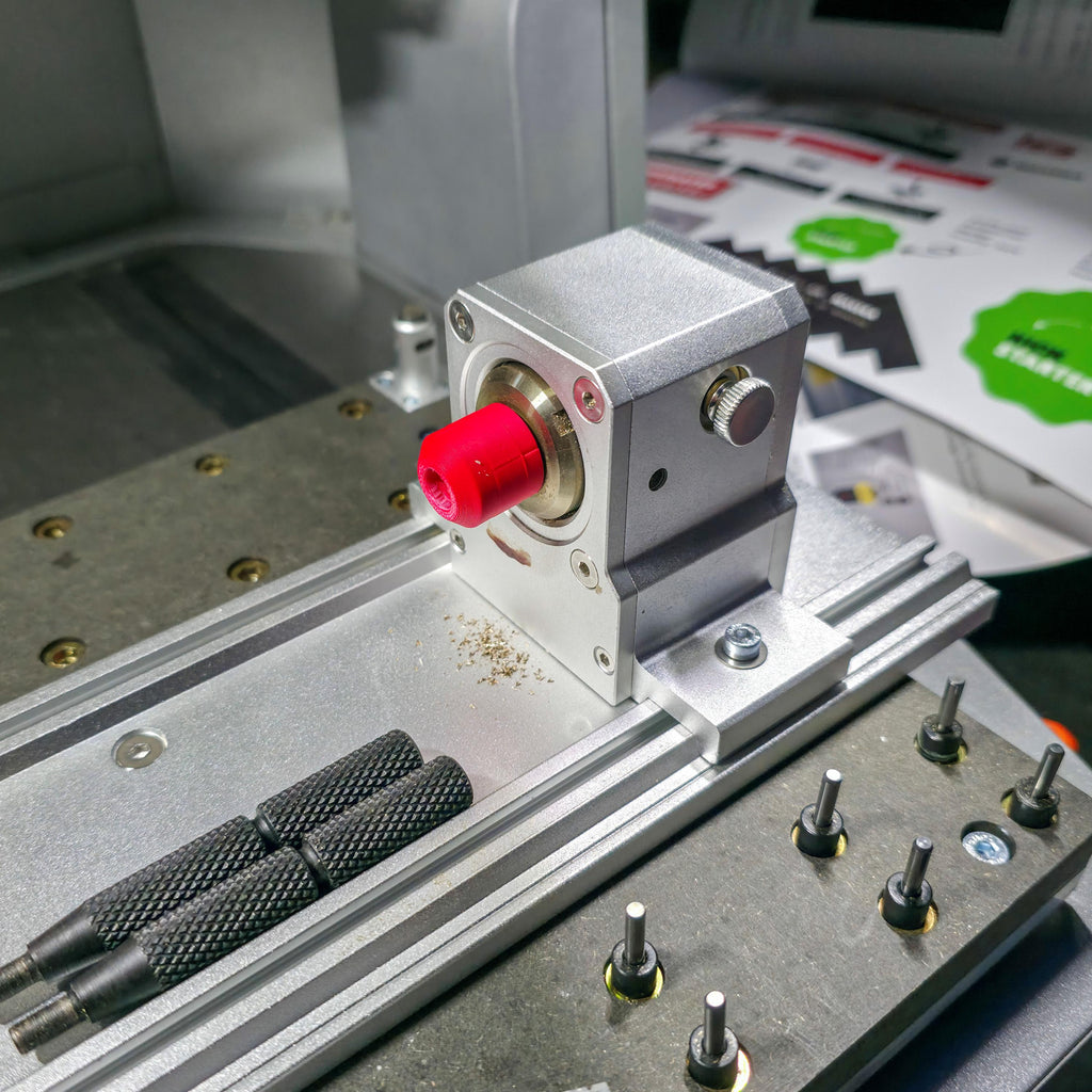 Side view of brass stock secured in a Makera 4th-axis head using a red precision jig. The smooth alignment shows accurate centering for rotary milling or engraving work.
