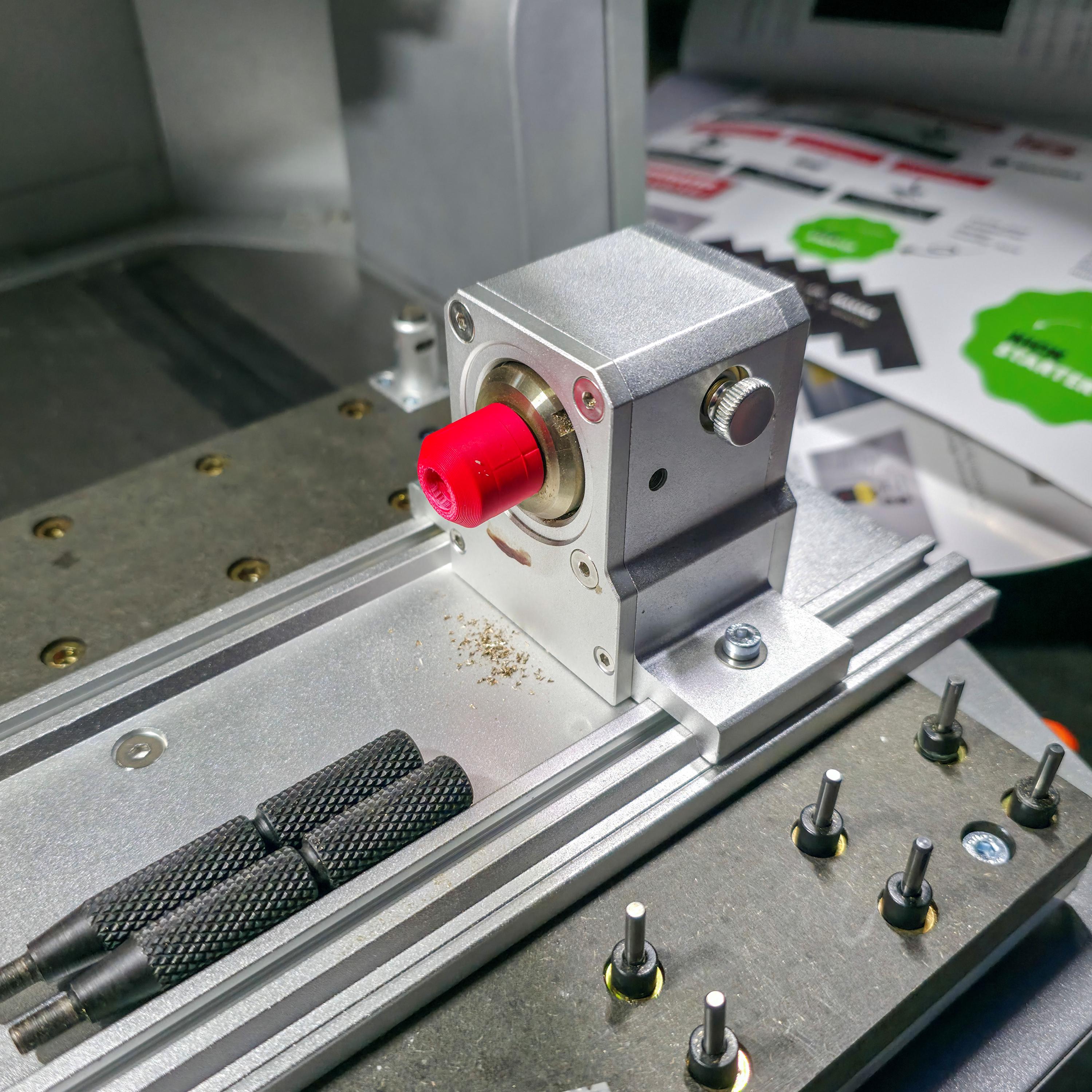 Side view of brass stock secured in a Makera 4th-axis head using a red precision jig. The smooth alignment shows accurate centering for rotary milling or engraving work.