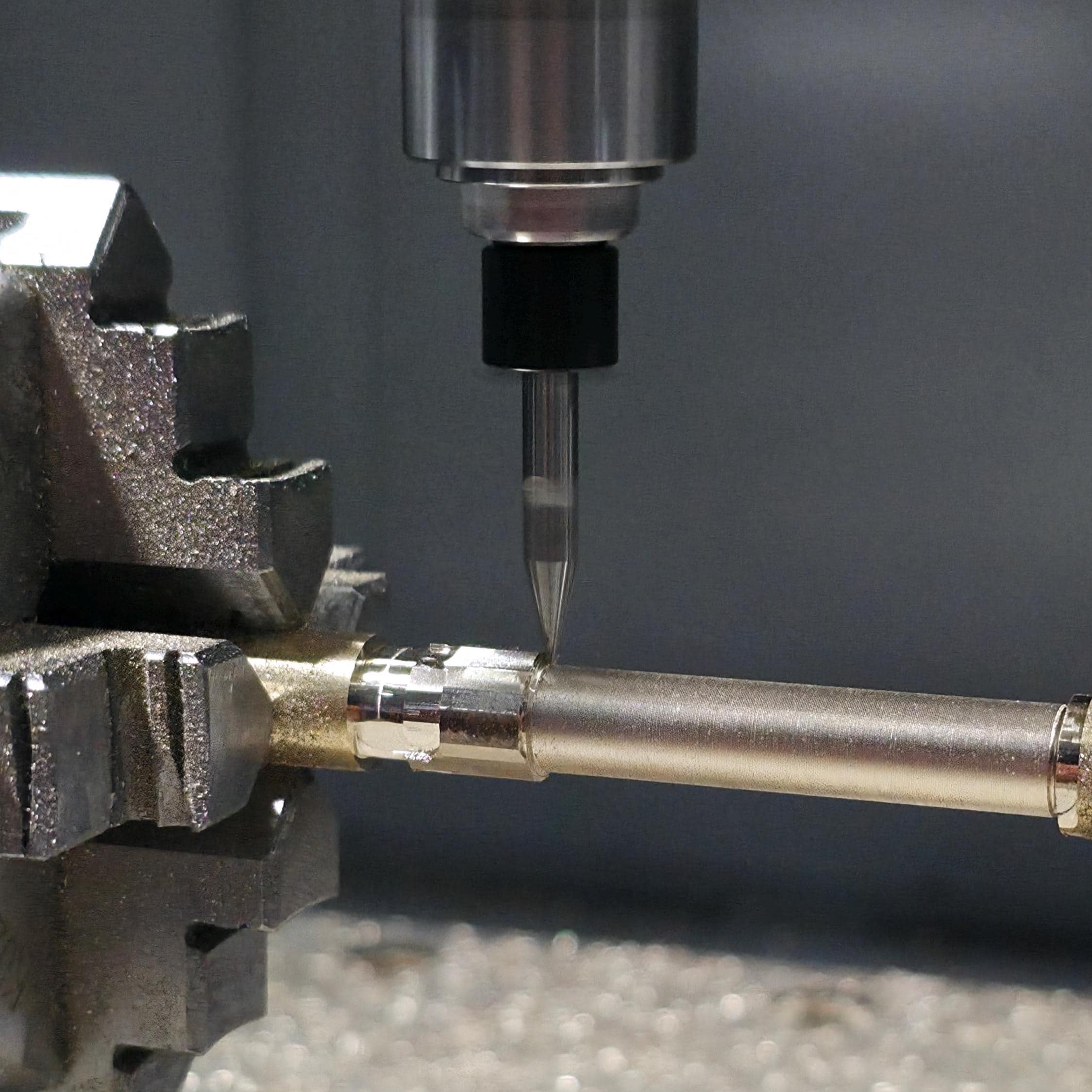 Close-up macro of CNC spindle tool engraving a brass rod held between two rotary chucks. Metal shavings reflect under bright workshop lighting, showing high-precision machining.