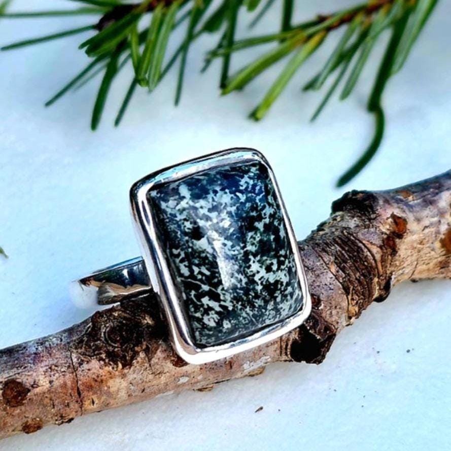 Image features an american handmade ring made out of sterling silver and a hand cut piece of nephrite jade from the north cascades of the PNW as the center stone. The artisan ring is on a white backdrop, with a nature motif. Symbolizing the aetherium brands connection to nature.