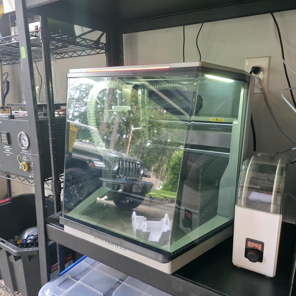 A Carvera Air CNC machine inside a clean, organized workshop setup with other fabrication tools. The reflective glass door and LED-lit interior highlight the precision workspace environment where the “OH SH*T BUTTON” might be used.