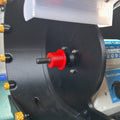 Close-up of the Cut n’ Cab V3 arbor adapter installed on a 10mm threaded shaft inside a modular lapidary grinder enclosure. The red adapter is centered and seated flush against a black motor mounting plate, designed to accept 1" wide Nova or diamond wheels. This offset-fit version corrects for short arbor shafts found on imported bench lathes and enables clean, balanced wheel mounting. Gold knurled knobs, part of the Cut n’ Cab system, are visible along the left side of the black housing.