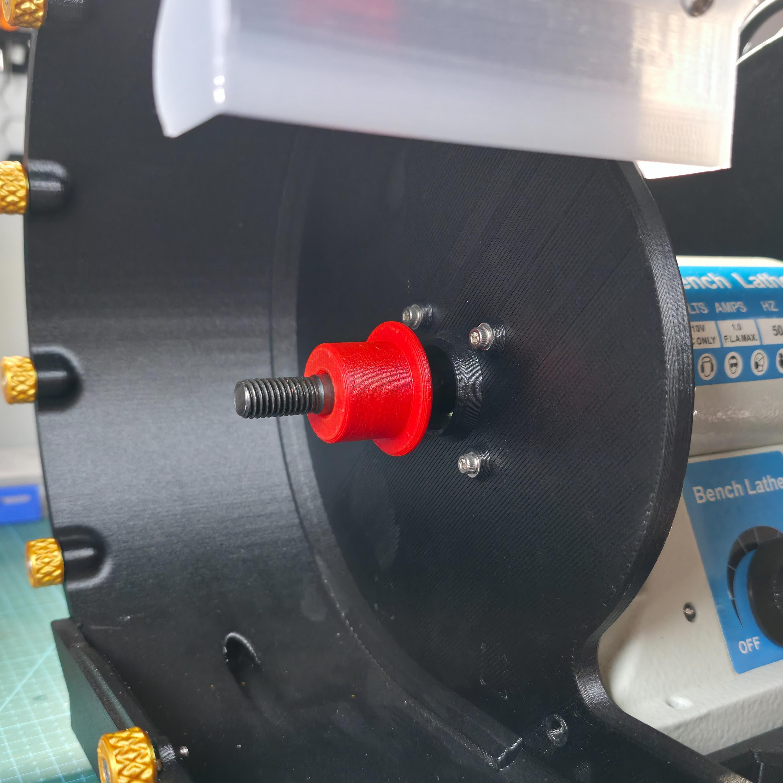 Close-up of the Cut n’ Cab V3 arbor adapter installed on a 10mm threaded shaft inside a modular lapidary grinder enclosure. The red adapter is centered and seated flush against a black motor mounting plate, designed to accept 1" wide Nova or diamond wheels. This offset-fit version corrects for short arbor shafts found on imported bench lathes and enables clean, balanced wheel mounting. Gold knurled knobs, part of the Cut n’ Cab system, are visible along the left side of the black housing.