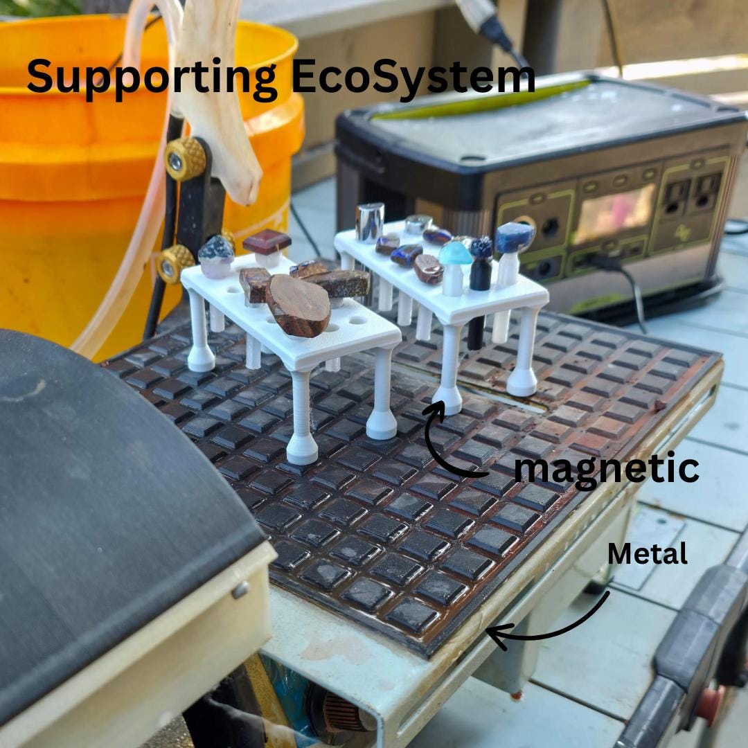 Multiple magnetic dop trays holding stones and dops placed on a cut n cab makerspace edition. Arrows indicate magnetic contact with steel, highlighting stability during wet grinding and polishing operations common in cabbing and faceting workflows.