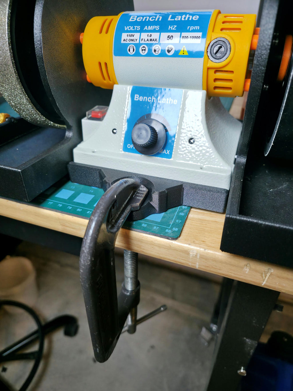 Bench lathe motor secured to a wooden workbench using the Aetherium Quick Clamp Adapter base with a metal C-clamp for portable mounting and vibration reduction.