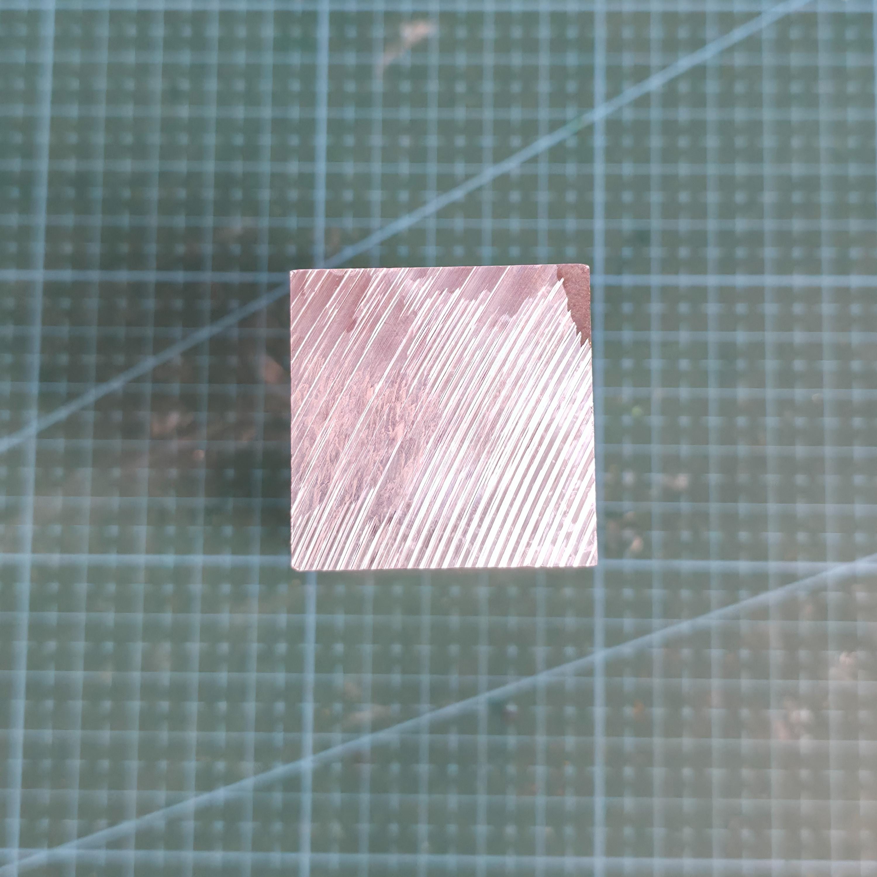 Square end of a 35×35×100 mm 6061-T6 aluminum bar shown on a cutting mat, displaying fresh diagonal CNC toolpaths. Ideal raw stock for machining drone mounts, brackets, precision prototypes, and small mechanical parts. Bright milled finish highlights the workable aluminum surface.