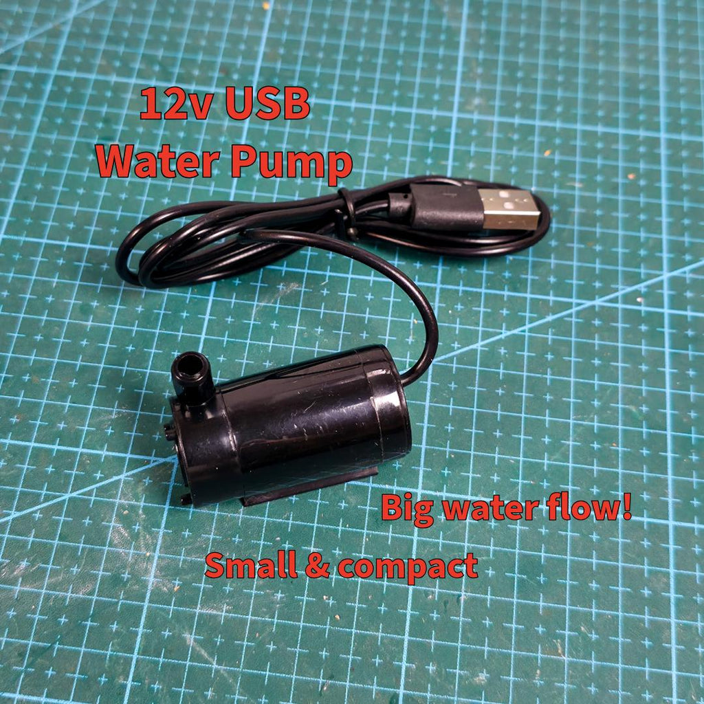 Close-up of a black USB-powered 12V water pump resting on a cutting mat. Text notes its high flow rate and compact size. This pump powers the MakerSpace Edition’s active water cooling system, suitable for portable use and small workspace setups.