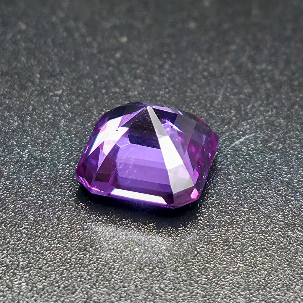 "A close-up of a faceted purple gemstone on a dark textured surface, capturing sharp facets and high brilliance. The gem exhibits rich violet tones, alexandrite, representing a finished result achievable with the Aetherium Gem Cutting Starter Kit tools."