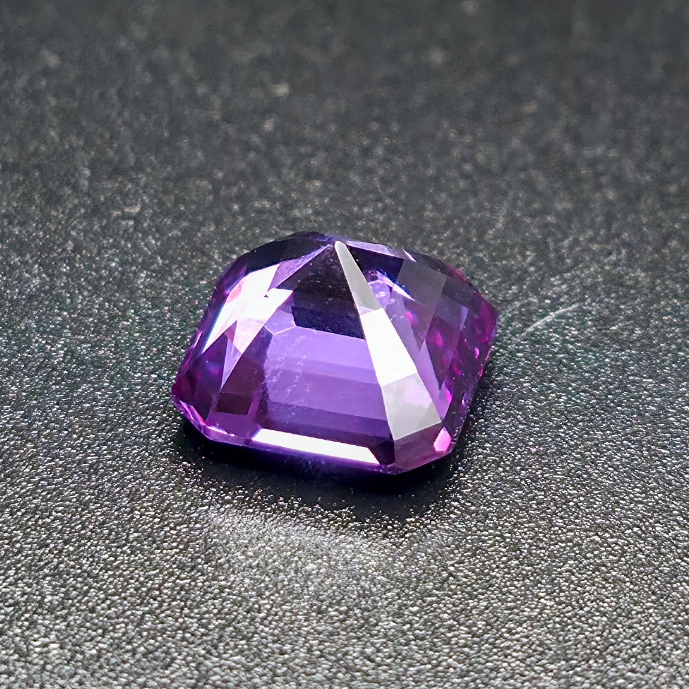 "A close-up of a faceted purple gemstone on a dark textured surface, capturing sharp facets and high brilliance. The gem exhibits rich violet tones, alexandrite, representing a finished result achievable with the Aetherium Gem Cutting Starter Kit tools."