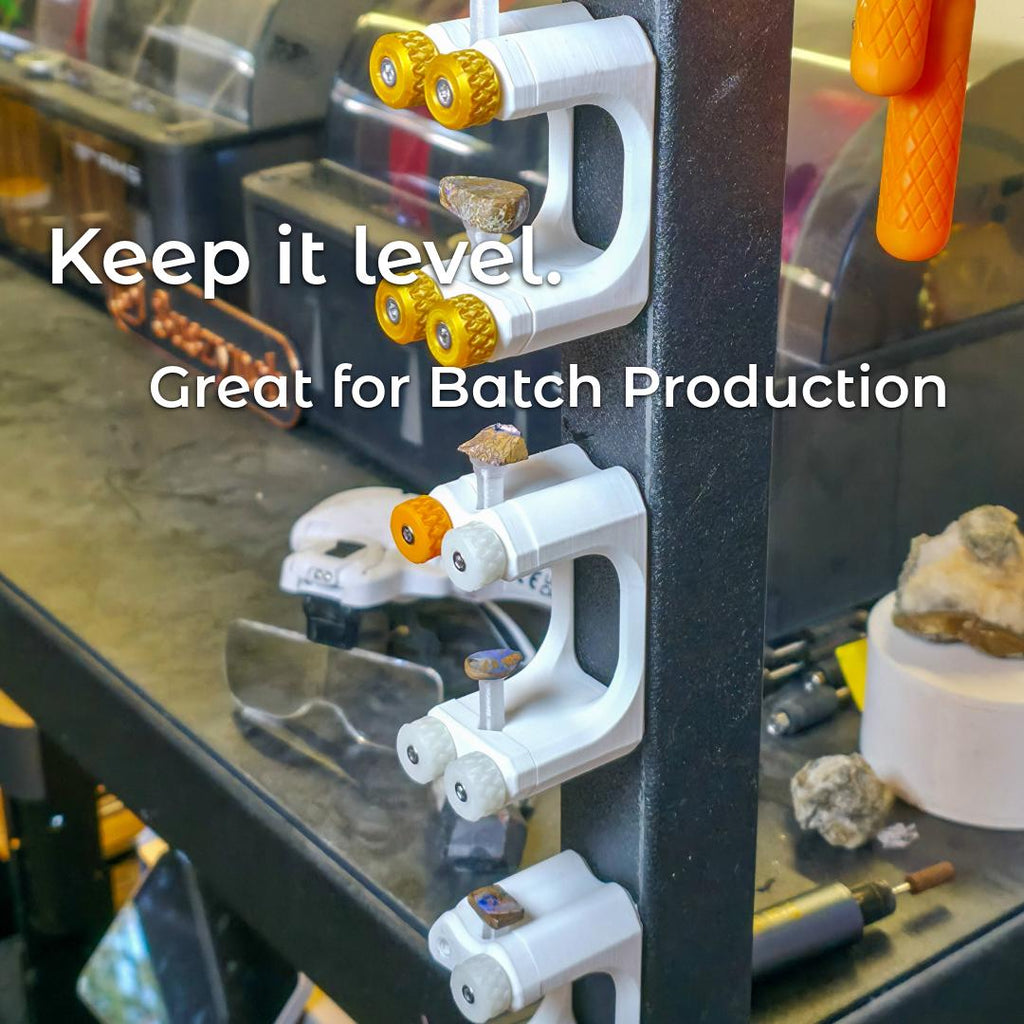 "Multiple Gem Xfer fixtures holding dop sticks with stones in various stages of cutting, mounted vertically on a metal workbench leg. The text overlay reads 'Keep it level. Great for Batch Production.' The image highlights alignment consistency and efficiency for gem cutting production runs."