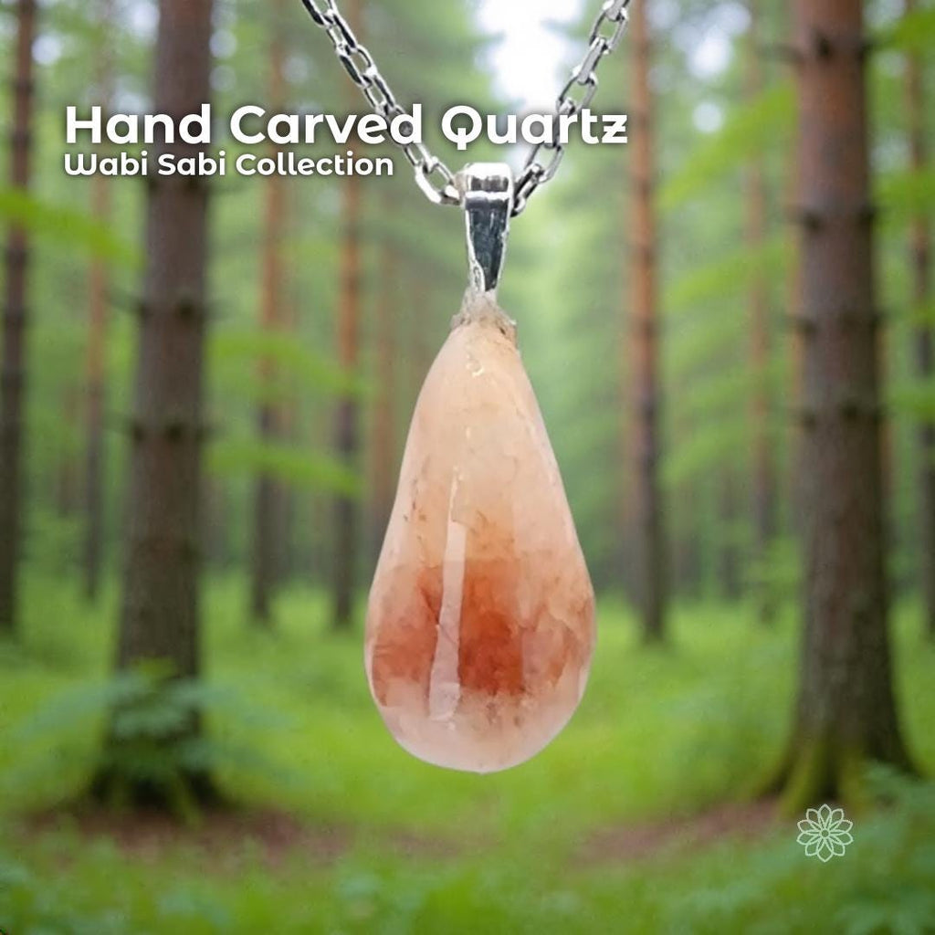 A hand-carved rose quartz pendant set in a sterling silver bail, hanging from a delicate silver chain in a soft green forest background. The stone is an organic teardrop shape with pale pink and warm reddish tones. Text on the image reads “Hand Carved Quartz – Wabi Sabi Collection,” with a small Aetherium floral mark in the lower right corner.
