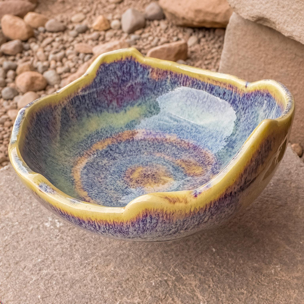 Close view of the Erosion Study No. 1 bowl showing its uneven, organic rim and swirling indigo-violet glaze over a yellow base. The matte-to-gloss finish reveals layered color gradients resembling erosion patterns. Hand-thrown, kiln-fired, food-safe ceramic made in the Pacific Northwest.