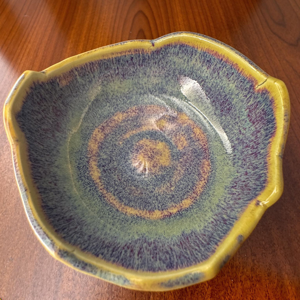 Overhead shot of the Erosion Study No. 1 pottery bowl on a wooden surface. Concentric rings of blue, violet, and gold glaze highlight its textured interior and natural asymmetry. A handmade, food-safe art piece for collectors or daily use, crafted by Seattle ceramicist Annie Archibald.