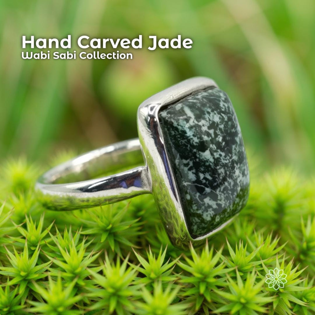 Hand carved nephrite jade ring with a dark green stone featuring white speckled patterns, set in a solid sterling silver band. The ring is photographed resting on bright green moss with soft blurred background foliage, emphasizing its natural, earthy, Pacific Northwest style.