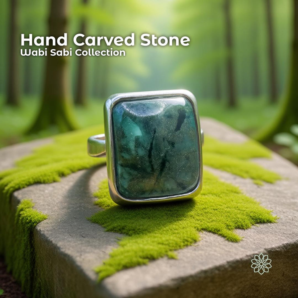 Hand carved chrysocolla cabochon ring with a dark blue-green raw stone set in a solid sterling silver band. The ring sits on a moss-covered stone in a lush forest setting, with soft green light and blurred trees in the background, highlighting its earthy, nature-inspired Pacific Northwest style.