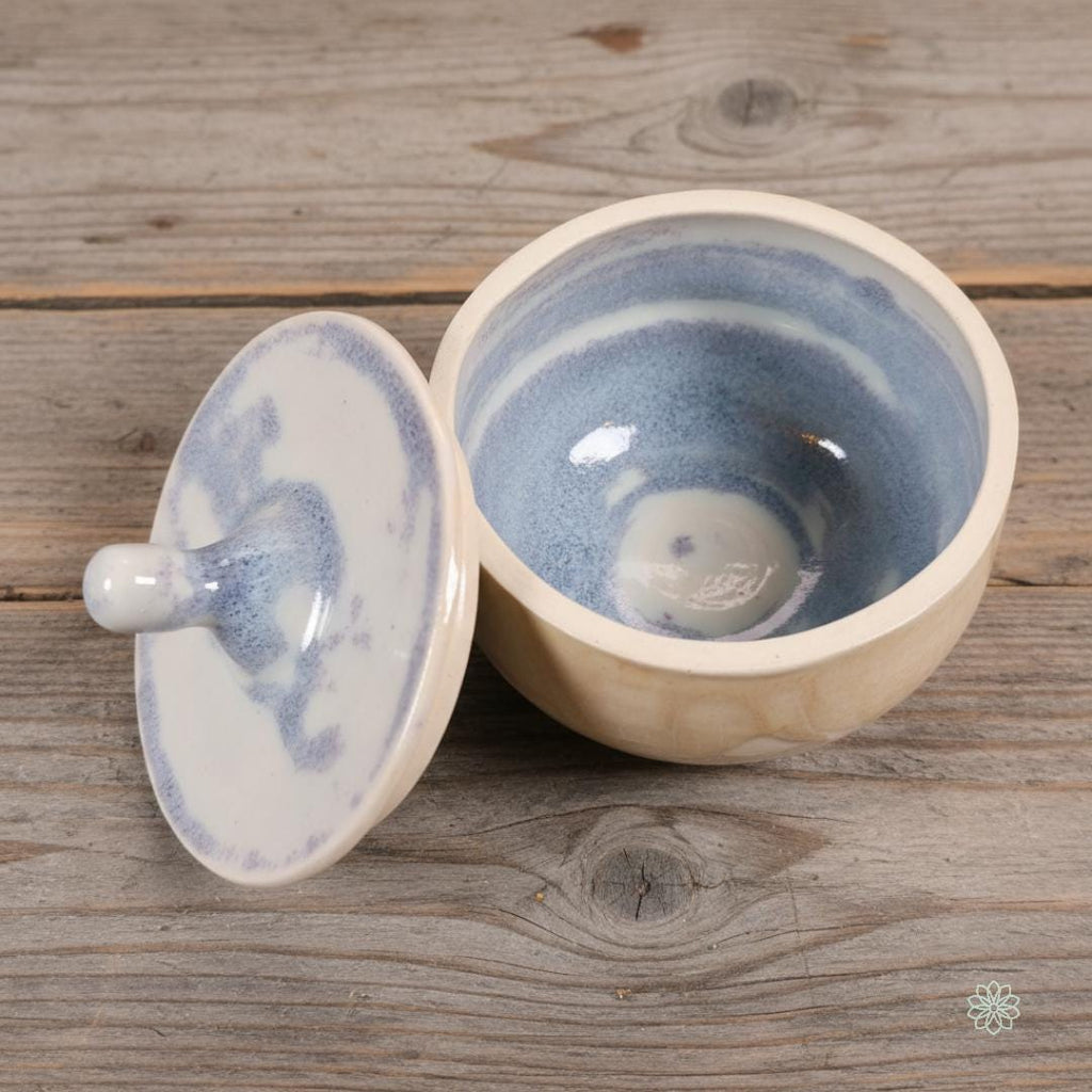“White and blue marbled ceramic altar jar with the lid placed beside the open bowl, showing glossy swirl glazing inside. Handmade pottery styled on rustic grey wood. Part of the Aetherium x Archibald altar jar set.”