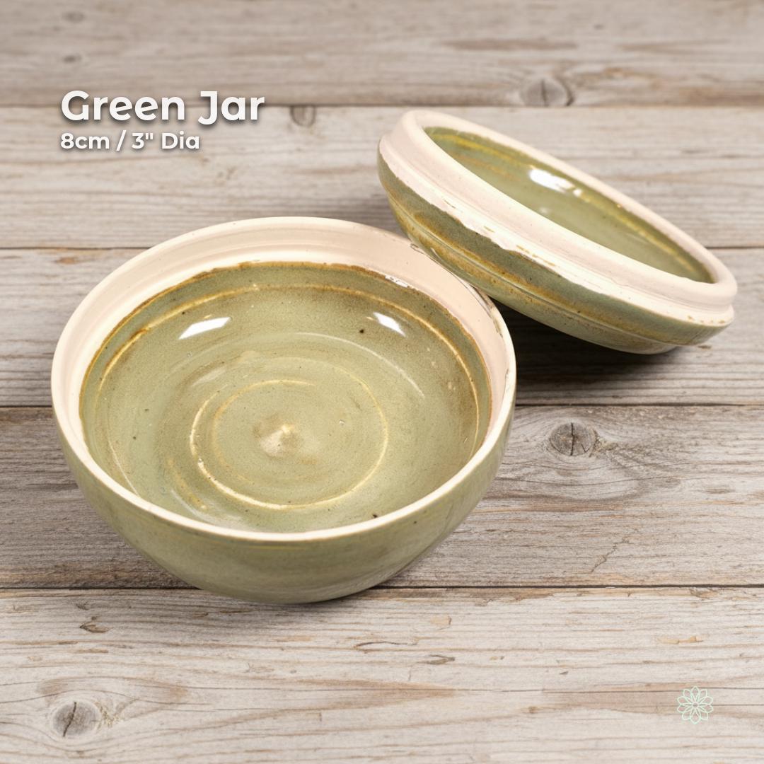 “Green glazed ceramic altar jar with the lid resting behind the bowl to show the interior. On-image text reads ‘Green Jar’ and ‘8cm / 3" Dia.’ Handmade stoneware shown on rustic grey wood.”