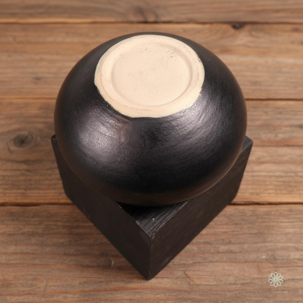 A close front view of the Rusty Bowl altar vessel on warm farmhouse wood. The exterior features layered smokey red, brown, and black glazes with a rounded, hand-thrown silhouette. No text overlays appear in this image. Part of the altar jar set offering.