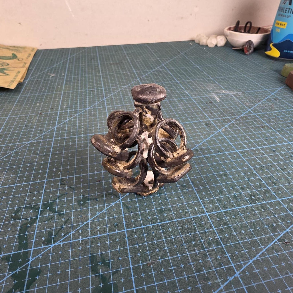 Studio photo of cast metal rings on a sprue base after burnout and pour. Surface shows oxidized texture and raw cast finish on cutting mat, demonstrating real-world output of the PolyCast process.