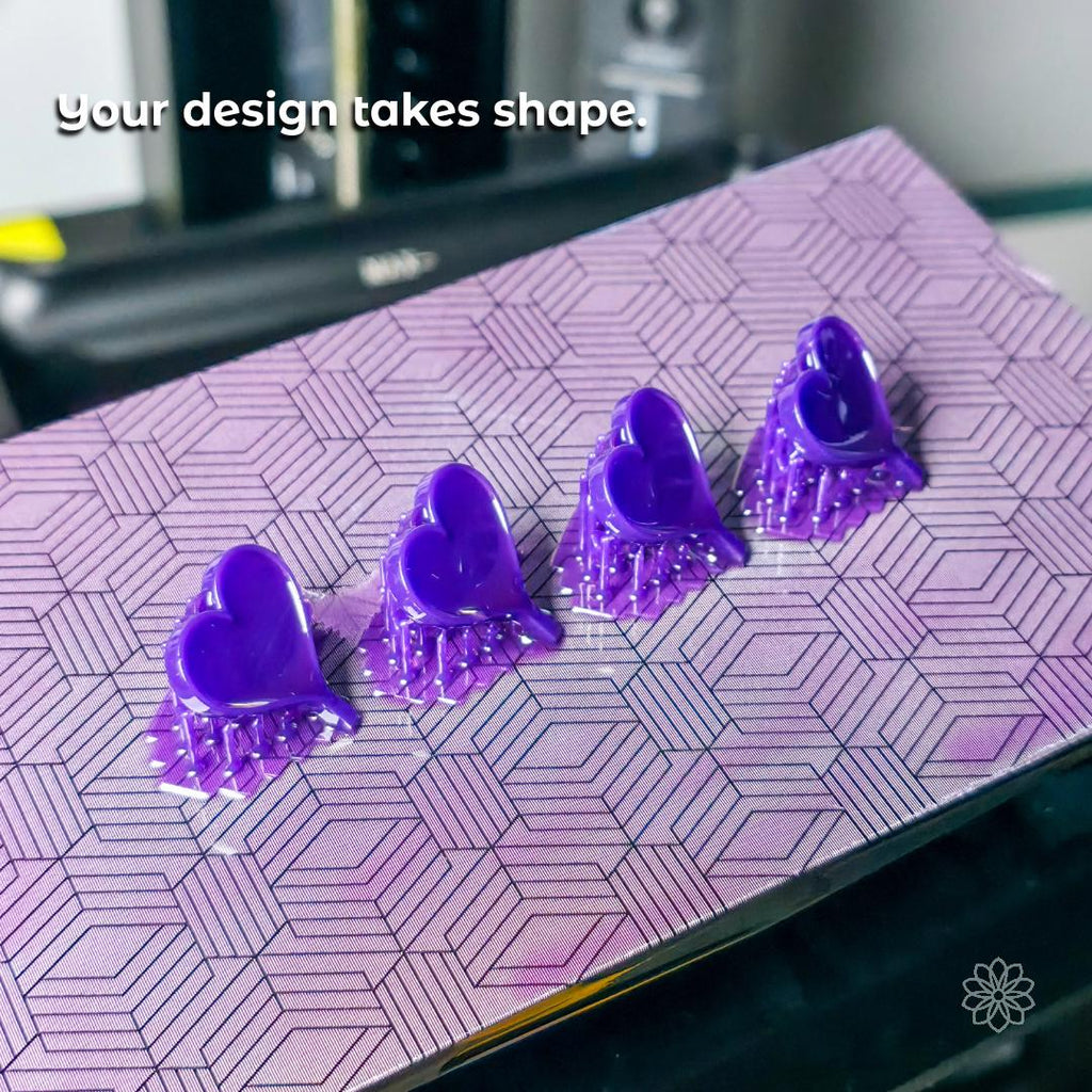 Row of purple resin heart models freshly printed on a textured build plate, showing the 3D printing phase of custom jewelry production. Demonstrates prototype creation, precision modeling, and readiness for lost-wax casting. Ideal for clients curious about how their concept becomes a physical form.