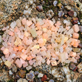 A cluster of UV-reactive calcite chips arranged on a polished agate slab. Warm orange and yellow calcite tones contrast with the banded agate surface. Lighting emphasizes translucency and fluorescence potential. Ideal for lapidary rough, resin inlay, carving practice, and mineral display. Scene showcases the material’s color saturation and internal structure.