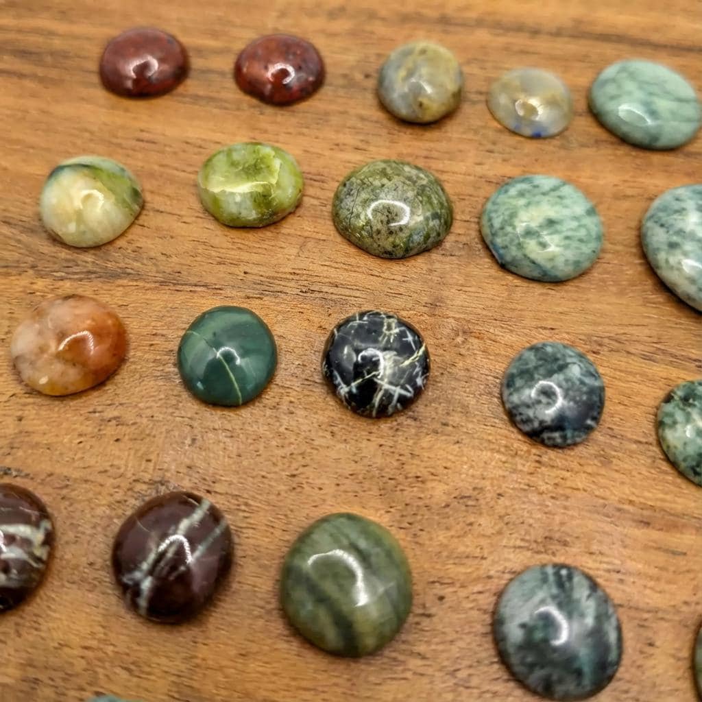 A varied collection of small cabochon gemstones arranged on a polished wood surface