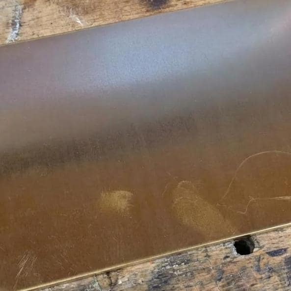 Detailed view of the brass sheet surface showing subtle color variation and natural handling marks under workshop lighting. The flat plate finish demonstrates consistent material texture appropriate for CNC milling, engraving, and finishing workflows where surface quality matters.