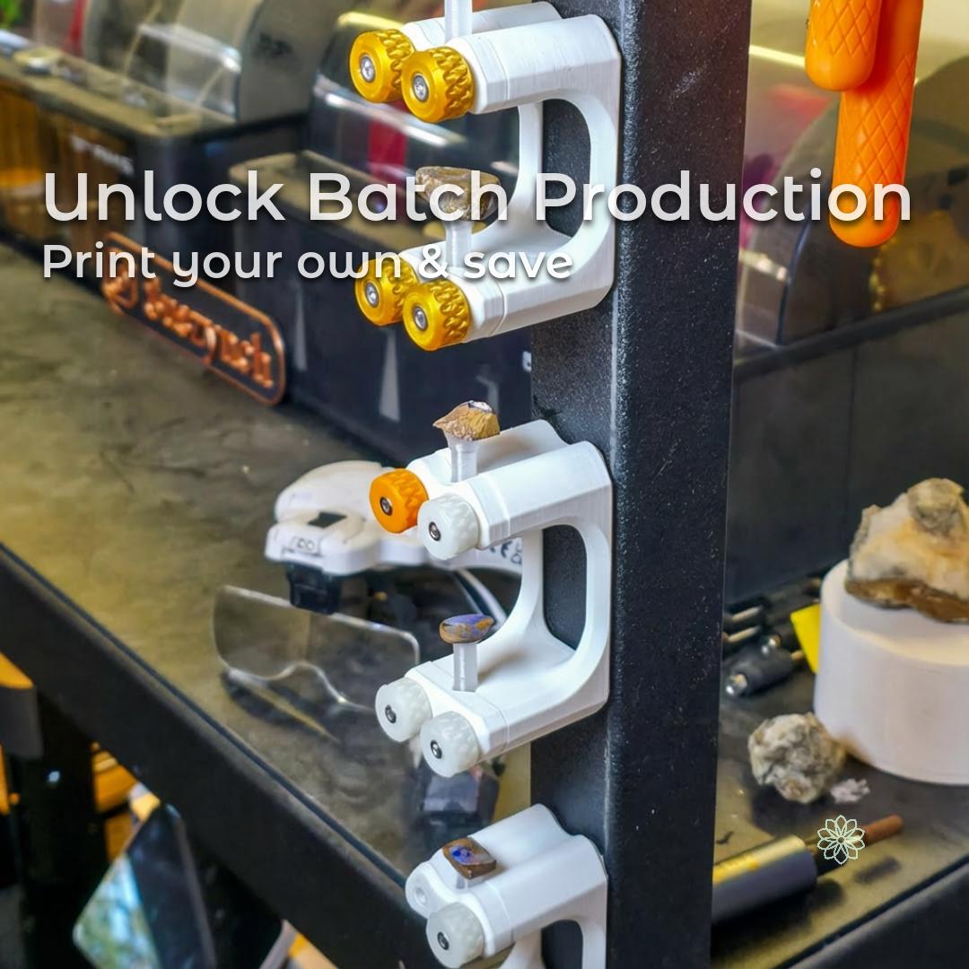 “Gem-Xfer epoxy cure station and transfer jig mounted vertically on a steel tool rack, each printed in white bioplastic with orange and white knurled knobs holding gemstone dops in place. Multiple units are stacked in a column to show batch production workflow for lapidary makers. Workshop benches, tools, and stones appear softly blurred in the background.”