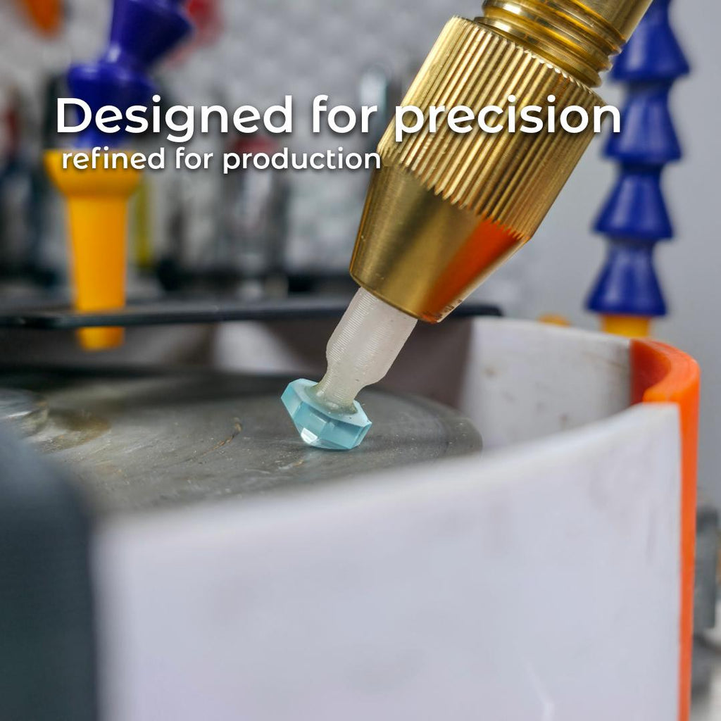 Close-up of a swiss blue topaz being cut on diamond lapidary disks. The brass quill and clear dop stick show how the 3D-printed version interfaces with faceting machines. Emphasizes precision fit and production-level repeatability for stone alignment.