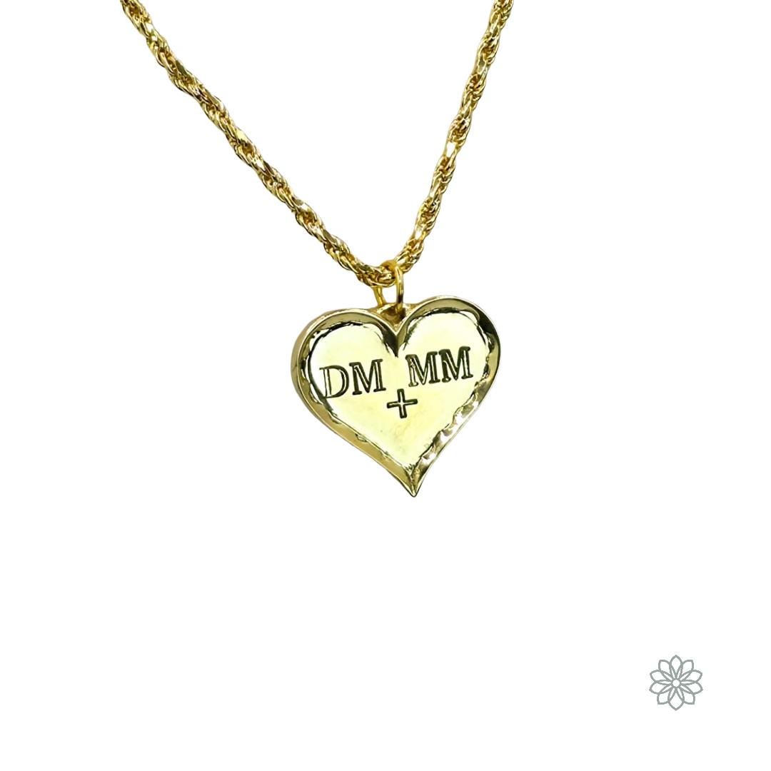 A polished engraved heart pendant made from solid brass, featuring two initials carved into the surface with a small loop at the top for attaching a chain. The pendant has a smooth reflective finish and rounded edges, shown against a clean white background to highlight its personalized, romantic style.