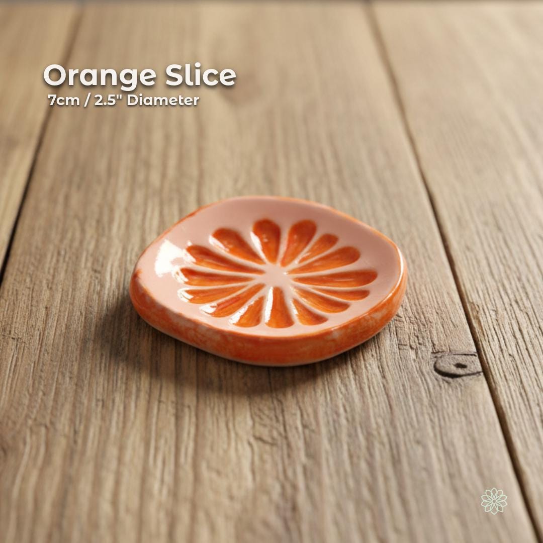 A small handmade ceramic dish shaped like a sliced orange, with hand-painted citrus segments in bright tangerine and peach glazes. Photographed on a soft-grain wooden surface with natural light that emphasizes its glossy finish and rounded edges. Ideal for jewelry, spices, tea bags, or gifting. Part of the Aetherium × Archibald small artisan dish collection.