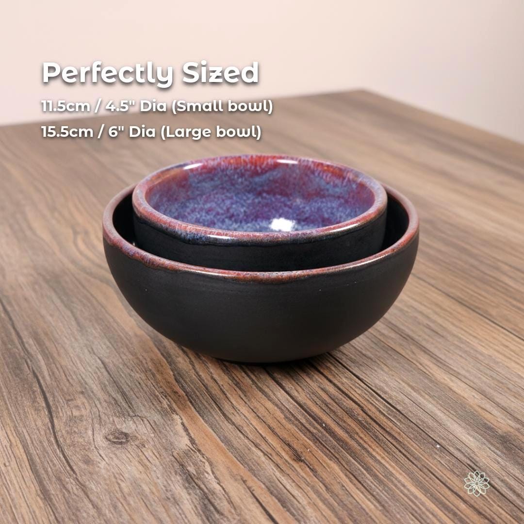 “Two handmade stoneware bowls shown stacked together. White text at the top reads ‘Perfectly Sized’ with size details below: ‘11.5 cm / 4.5” Dia (Small bowl)’ and ‘15.5 cm / 6” Dia (Large bowl)’. The bowls have matte black exteriors and purple-blue reactive glaze interiors. Displayed on a warm wood grain tabletop with the Aetherium × Archibald logo in the lower right.”
