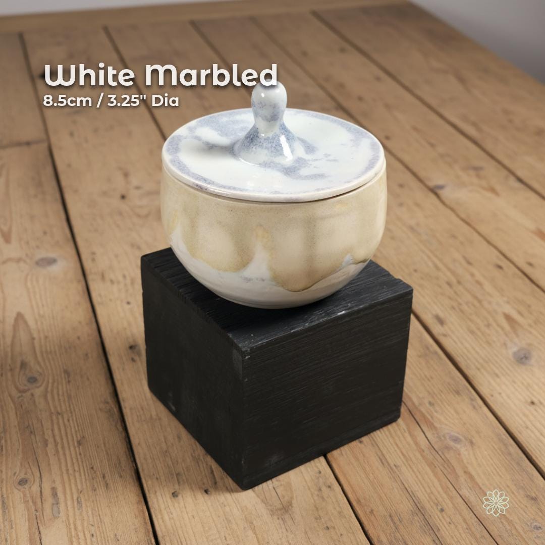 “White marbled ceramic altar jar resting on a black block. On-image text reads ‘White Marbled’ and ‘8.5cm / 3.25" Dia.’ Smooth rounded lid with sculpted handle. Displayed on light wood surface.”