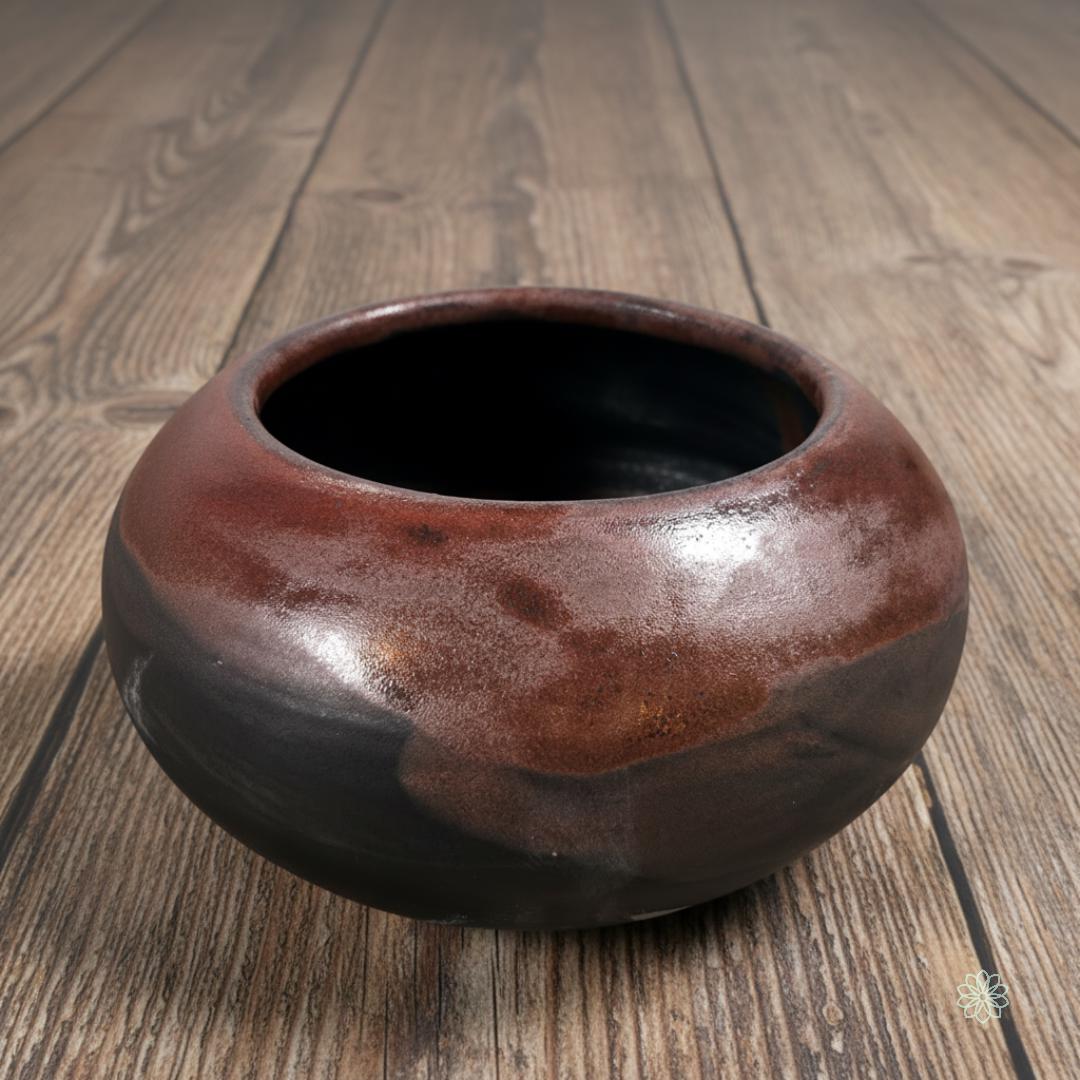 “Reactive-glaze brown ceramic altar bowl with deep rounded shape and a black interior. Shown on warm farmhouse wood. Part of the Aetherium x Archibald altar vessel collection.”