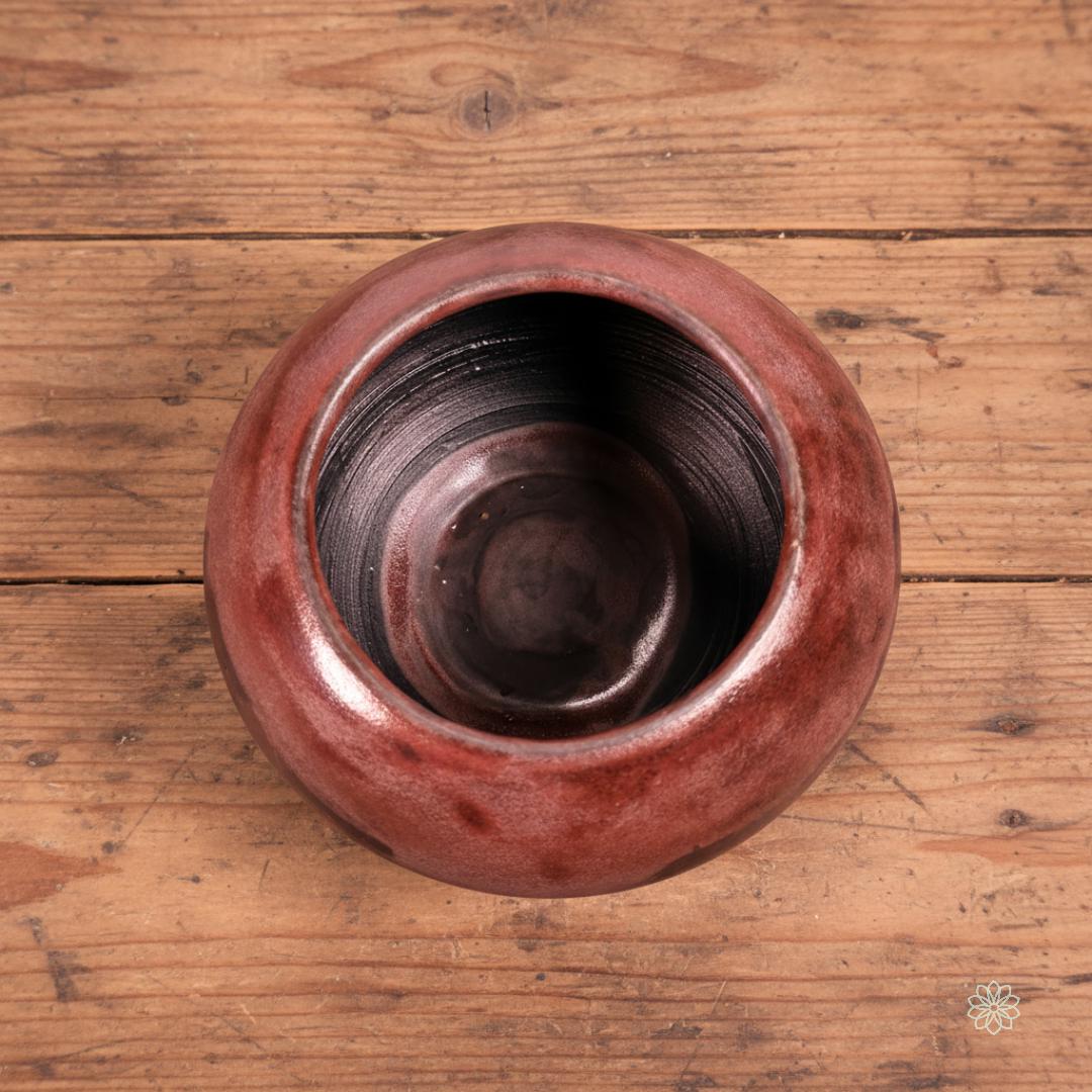 Top-down view of the Rusty Bowl, showing its smooth black interior and rounded rim with mottled rust and charcoal glaze. The bowl sits on aged wooden planks. This open-form vessel is the “Rusty Bowl” variation, approx. 10 cm / 4 inches diameter.