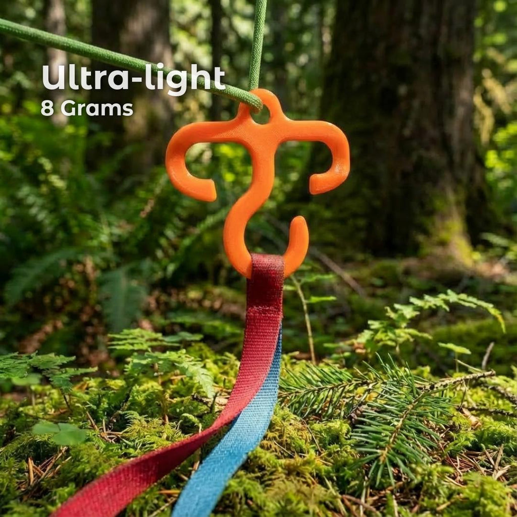 Orange ultralight mini hook clipped to a green paracord line holding a red and blue webbing strap. Forest ground below with moss and ferns highlights the compact, low-weight gear function for backpackers.