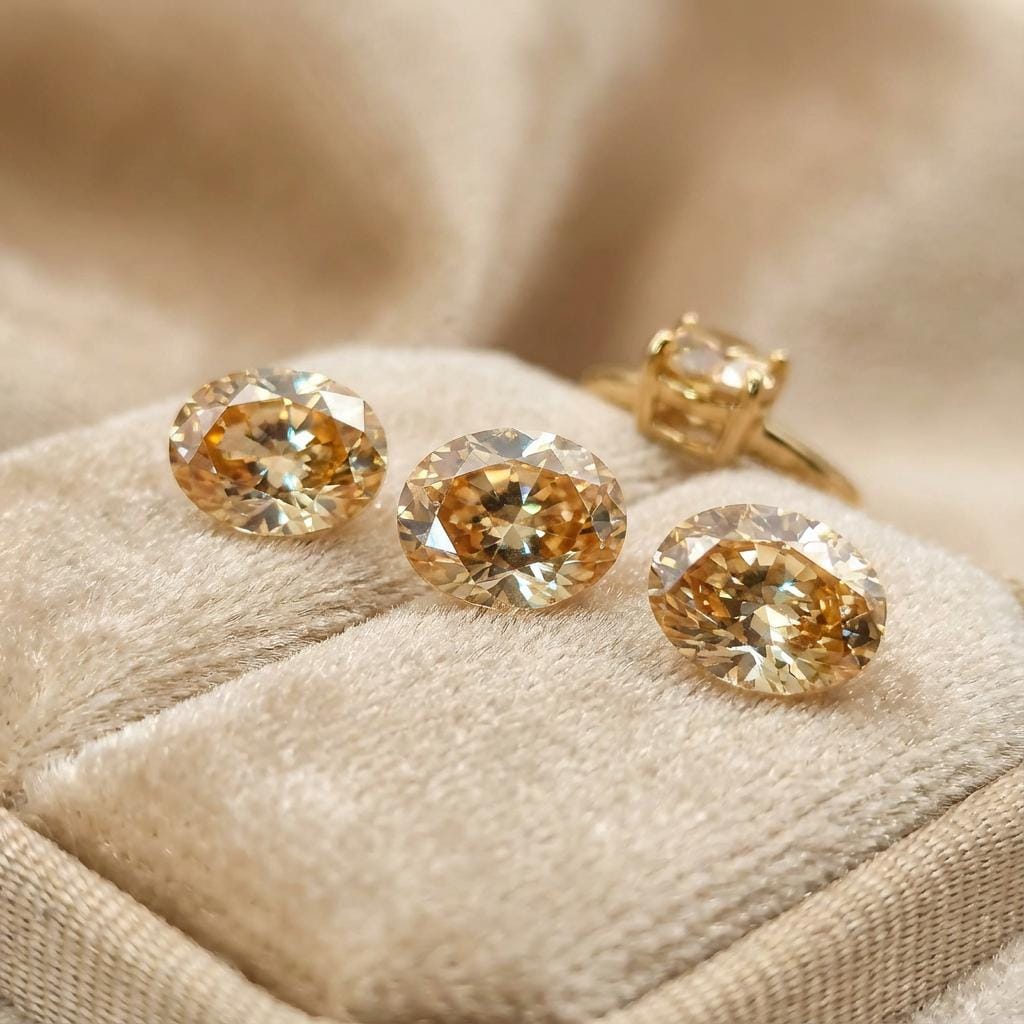 “Three oval-cut champagne cubic zirconia gemstones displayed on a soft beige jewelry tray, with a gold ring in the background. The stones show bright faceting, warm golden sparkle, and calibrated 9×7 mm proportions, ideal for custom rings, pendants, and fine jewelry design.”