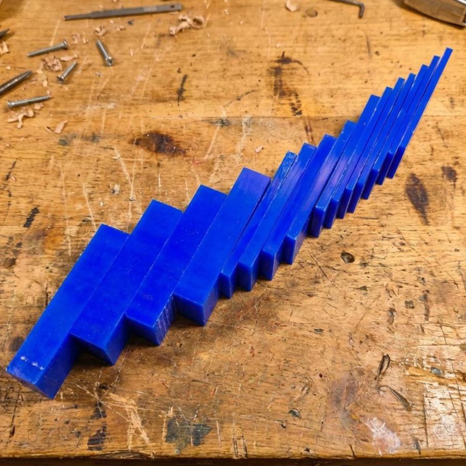 Staggered stack of blue jeweler’s carving wax pieces on a scratched bench surface. The blocks show clean edges and uniform density, perfect for wax lathes, flex-shaft shaping, or multi-piece casting model fabrication.