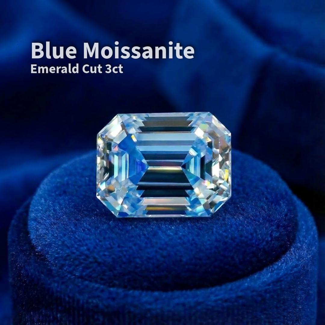 A 3 carat emerald-cut blue moissanite displayed face-up on deep blue velvet. The stone shows clean step facets, a centered table, and balanced symmetry. Color appears cool blue with high clarity and controlled dispersion. The rectangular emerald cut emphasizes depth, geometry, and mirror-like light return, suitable for precision jewelry settings or custom design work.