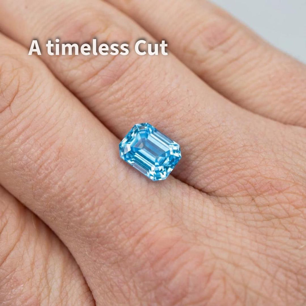 A 3 carat emerald-cut blue moissanite resting on a fingertip to show real-world scale. The rectangular proportions and step facets emphasize a calm, deliberate brilliance. This image helps visualize size, orientation, and wearability for rings or pendants while maintaining focus on cut precision rather than sparkle exaggeration.